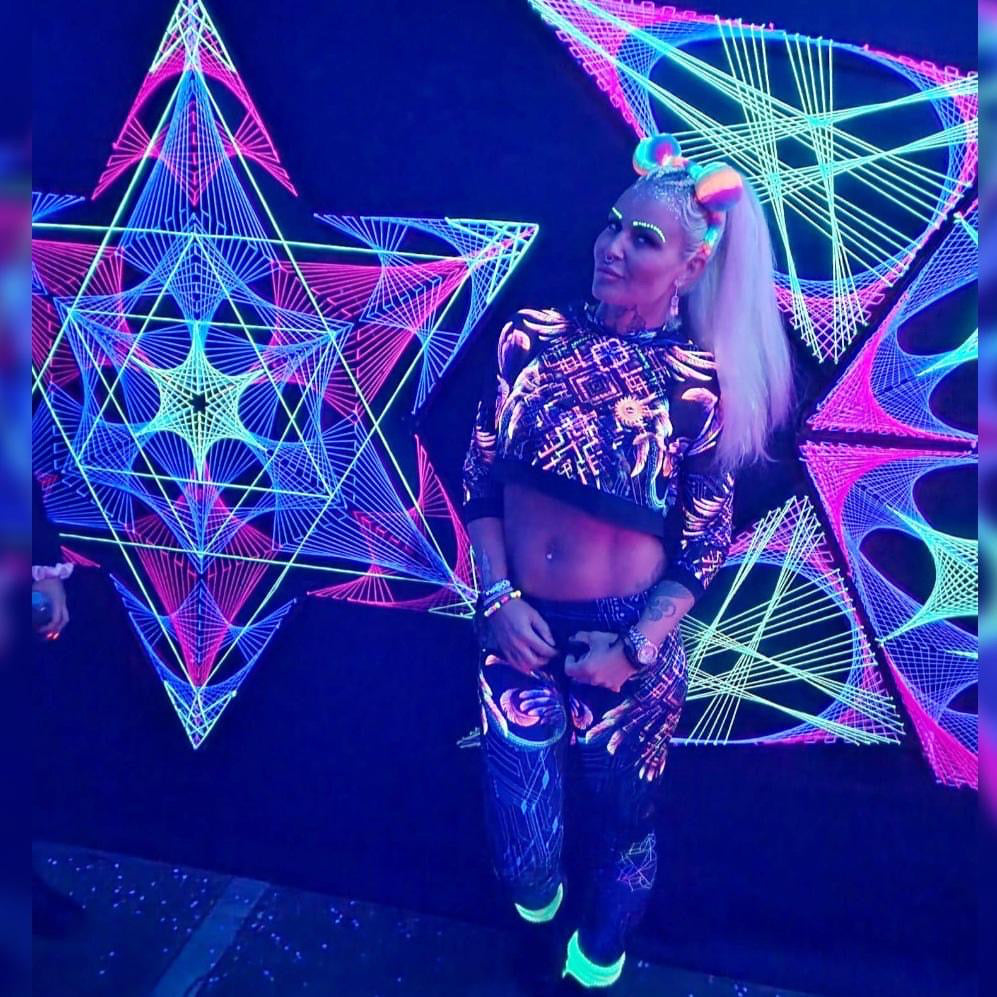 Raver wearing uv reactive art clothing and posing next to uv reactive string art installation