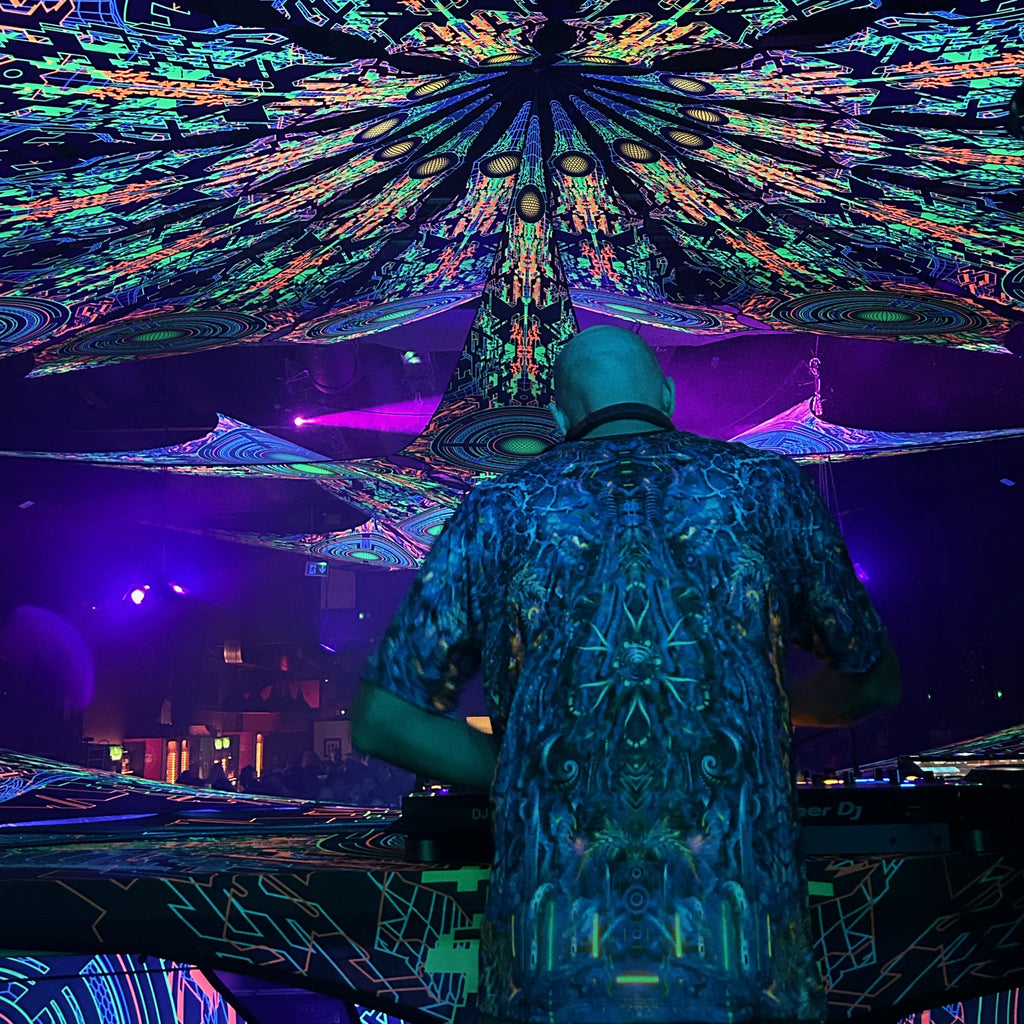 DJ on stage wearing a t-shirt T-shirt with UV-reactive psychedelic art print glowing under blacklight 